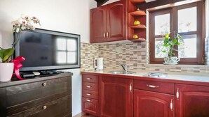 Una cocina con gabinetes de madera, salpicadero de azulejos, un ventanal con vistas y un televisor de pantalla plana sobre un mueble de madera.