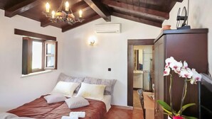 Un dormitorio con techo de madera, una cama con colcha roja, una mesita de noche, un espejo y una orquídea en maceta.