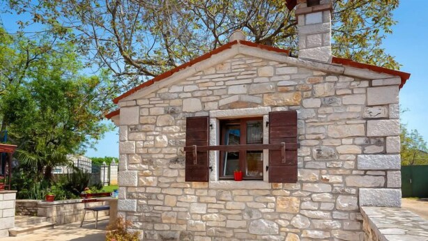 Un edificio de piedra con una ventana pequeña y contraventanas, un banco y plantas en macetas.