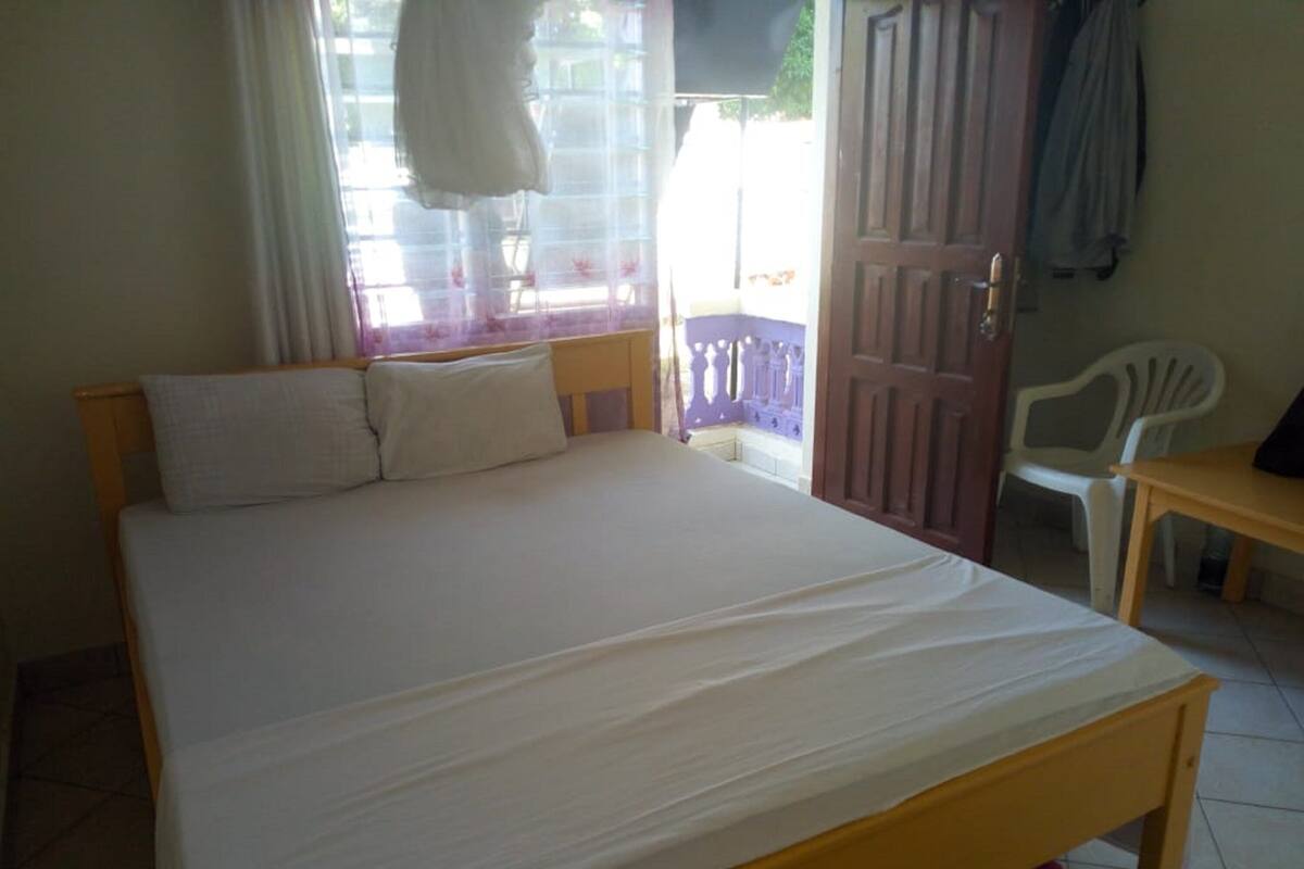 Quarto com cama, cadeira, mesa e porta que dá para o exterior.