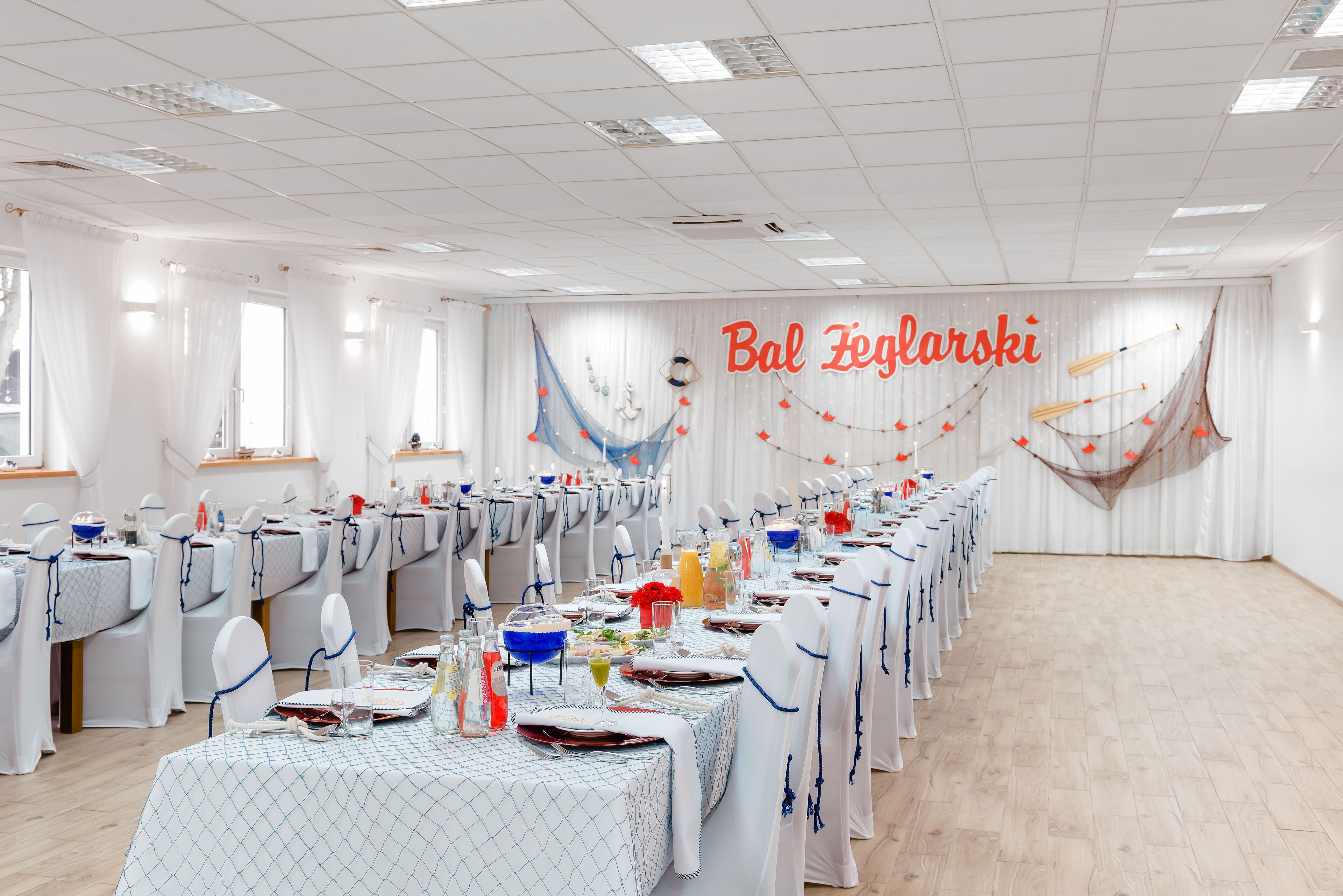 A banquet hall with tables set for a formal event, white drapery, and a banner reading "Bal Feglarski".