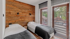 Een slaapkamer met twee bedden, houten wandpanelen en grote ramen met zonwering.