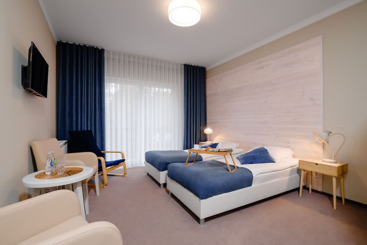 A hotel room with two beds, a desk, a chair, a TV, and a large window with curtains.