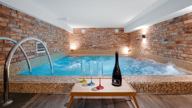Een bubbelbad met een bakstenen muur, een zwembad en een tafel met glazen en een fles.