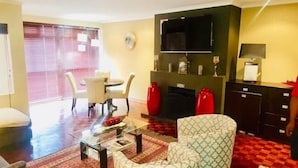 Uma sala de estar com sofá, mesa de centro, TV instalada acima da lareira e um espaço de jantar com cadeiras e mesa.
