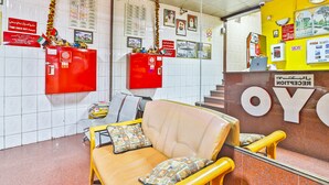 A reception area with a red desk, a beige sofa, and a yellow wall with a clock. - Oyo 393 Al Wehda Hotel (Dubai)