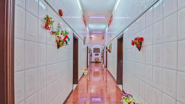 A corridor with white tiled walls, a shiny tiled floor, and hanging flower baskets. - Oyo 393 Al Wehda Hotel (Dubai)
