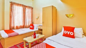 A hotel room with two single beds, a wooden wardrobe, a small table with a red and white patterned table runner, a red and white throw blanket, a red and white pillow with the word "OYO" on it, a red and white patterned rug, and a window with curtains. - Oyo 393 Al Wehda Hotel (Dubai)