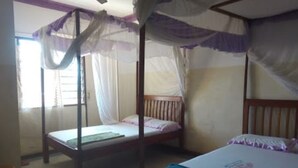 A room with two single beds, each with a wooden frame and a mosquito net.