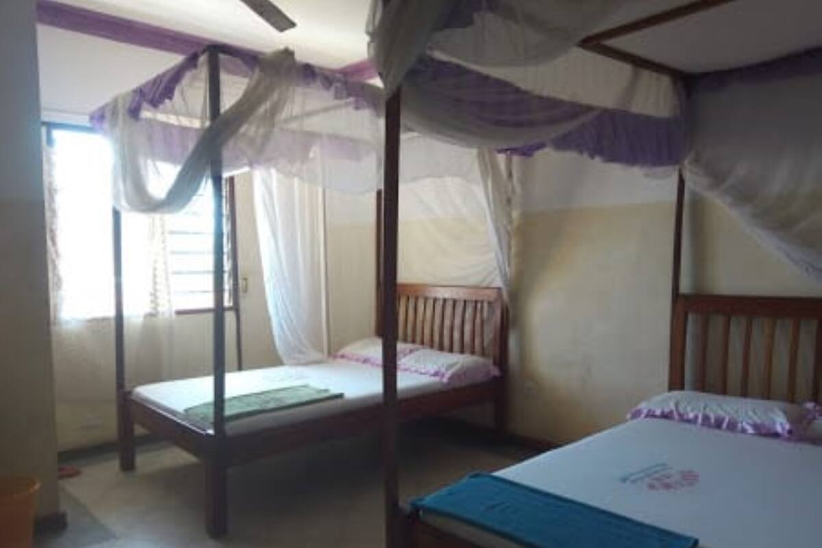 A room with two beds, one with a canopy and one without, a wooden headboard, and a window with curtains.