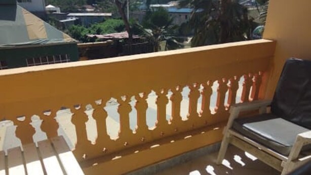 A balcony with a wooden railing, a single chair, and a view of buildings and trees in the background.