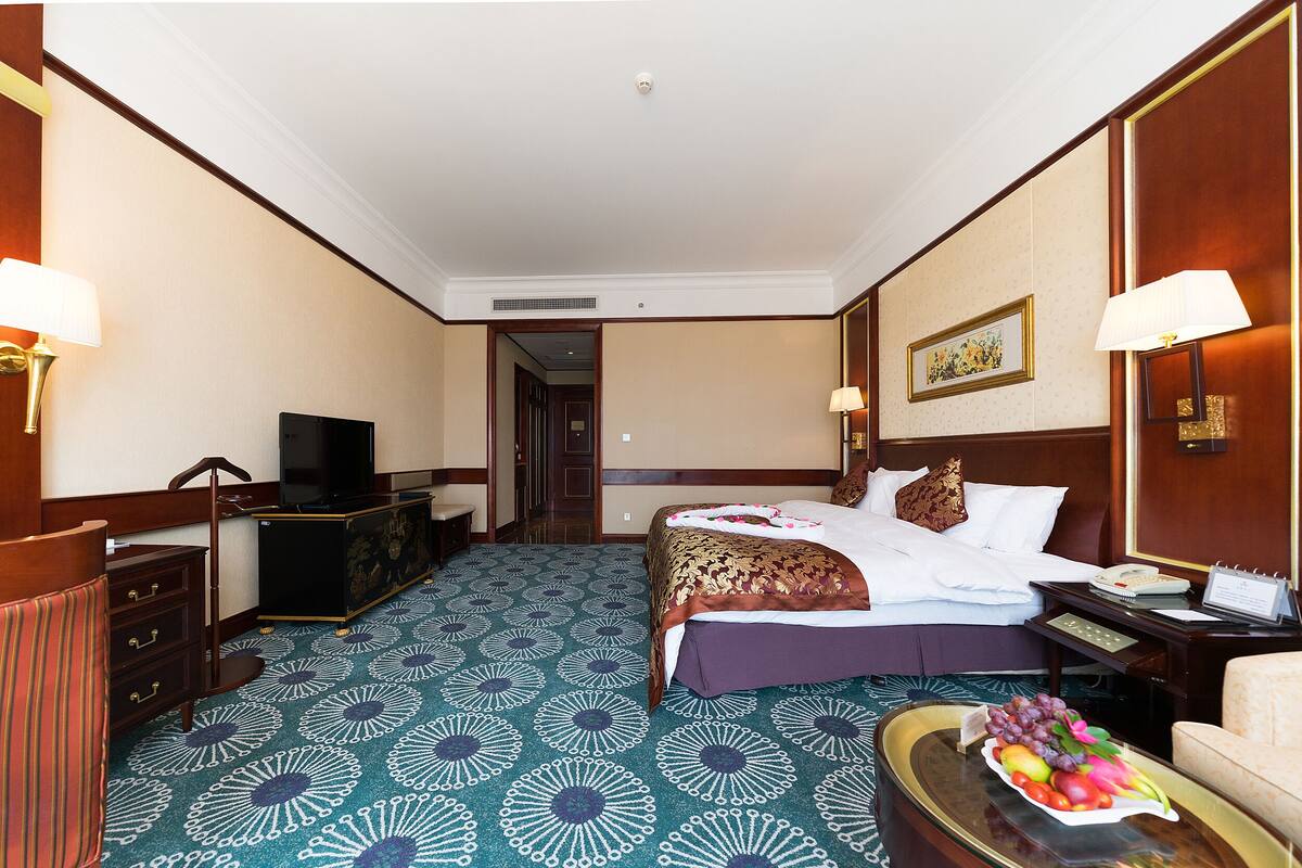 A hotel room with a bed, bedside tables, a desk, a television, and a fruit basket on the floor.