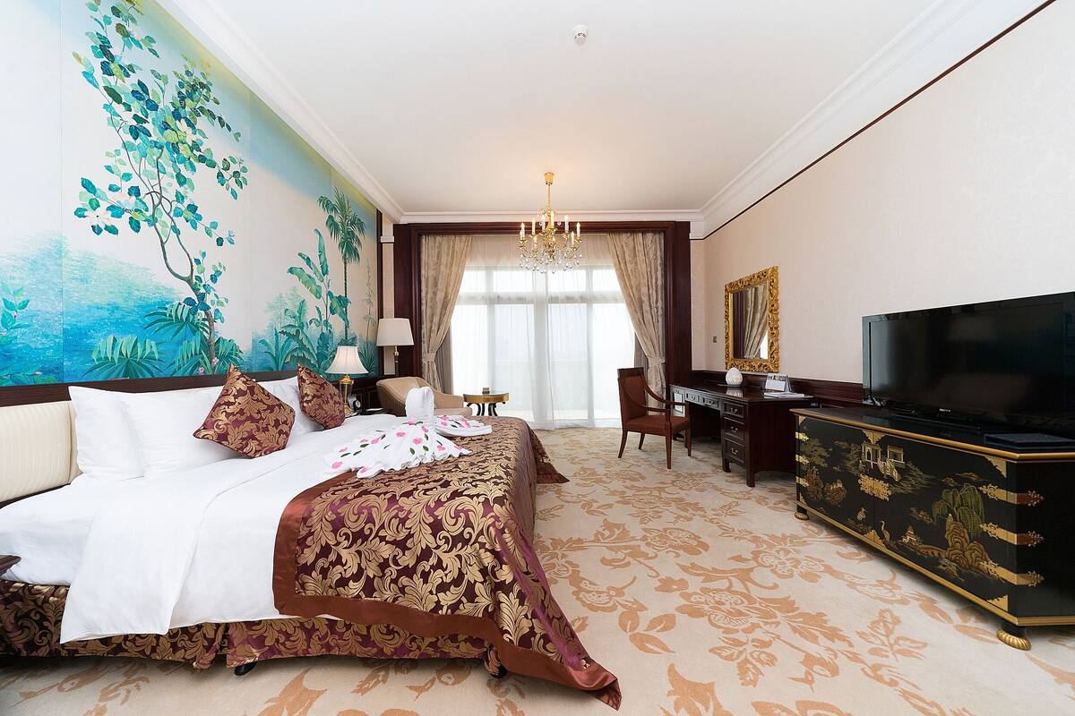A hotel room with a large bed, a desk with a television, and a mural on the wall.