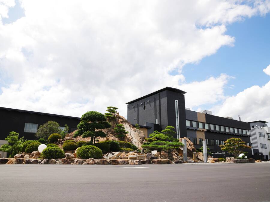 A modern building with a landscaped garden featuring rocks, shrubs, and a prominent tree.