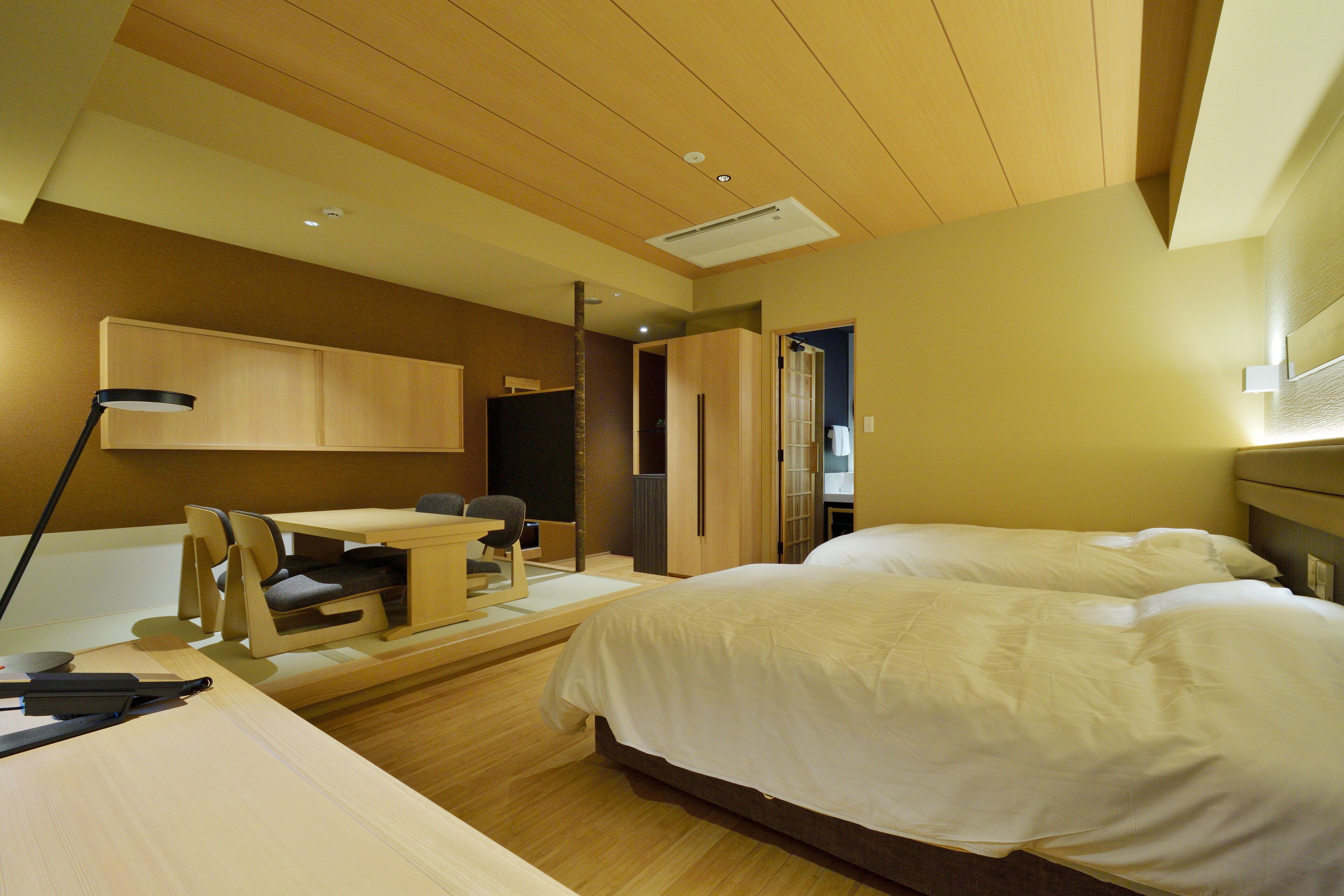 Una habitación de hotel moderna con techo de madera, un escritorio con sillas, una cama y un armario.