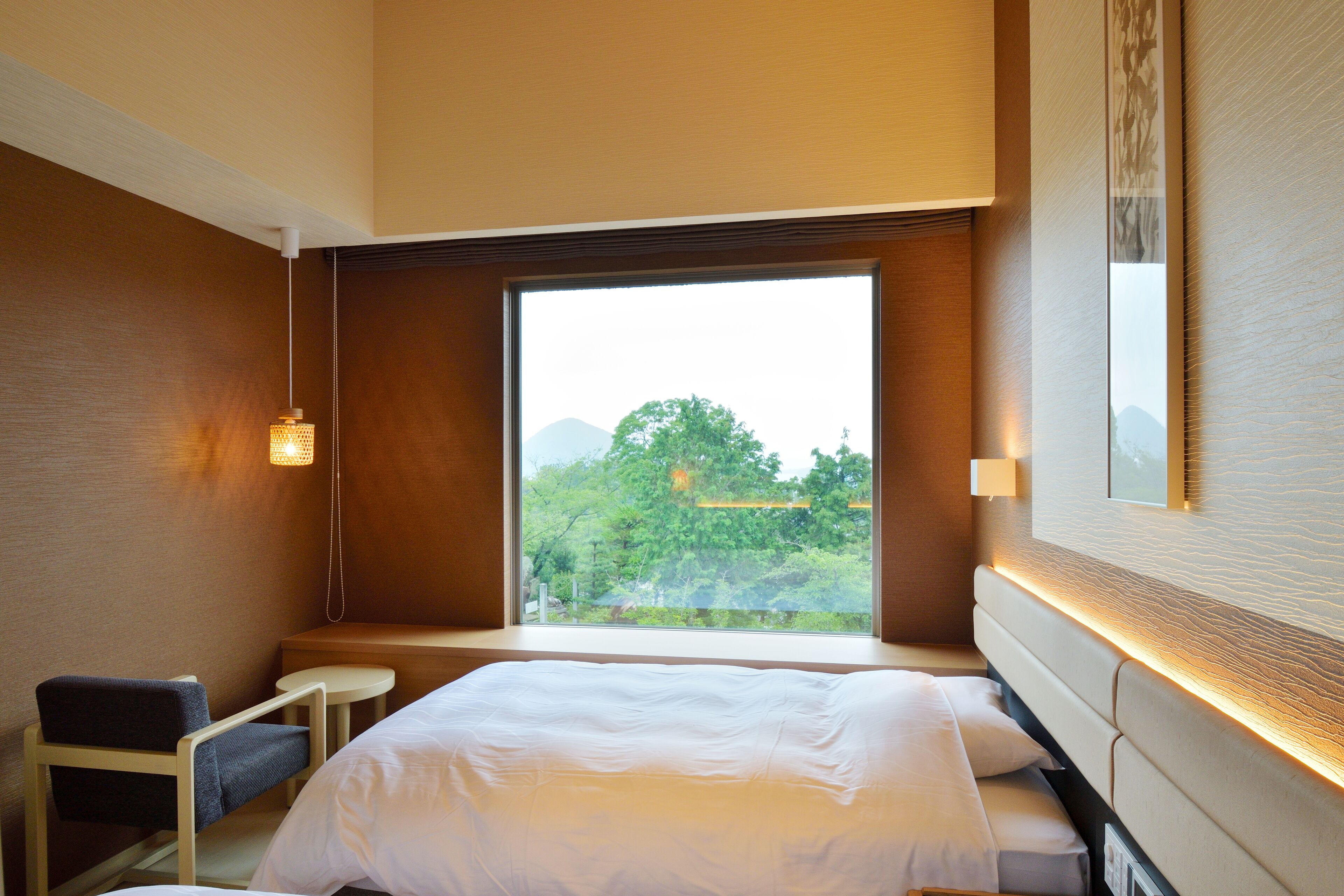 A hotel room with a large window, a bed, a chair, and a small table.