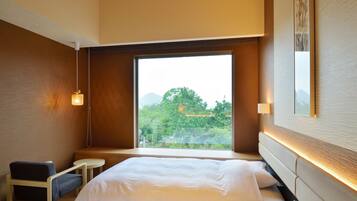 A hotel room with a large window, a bed, a chair, and a small table.
