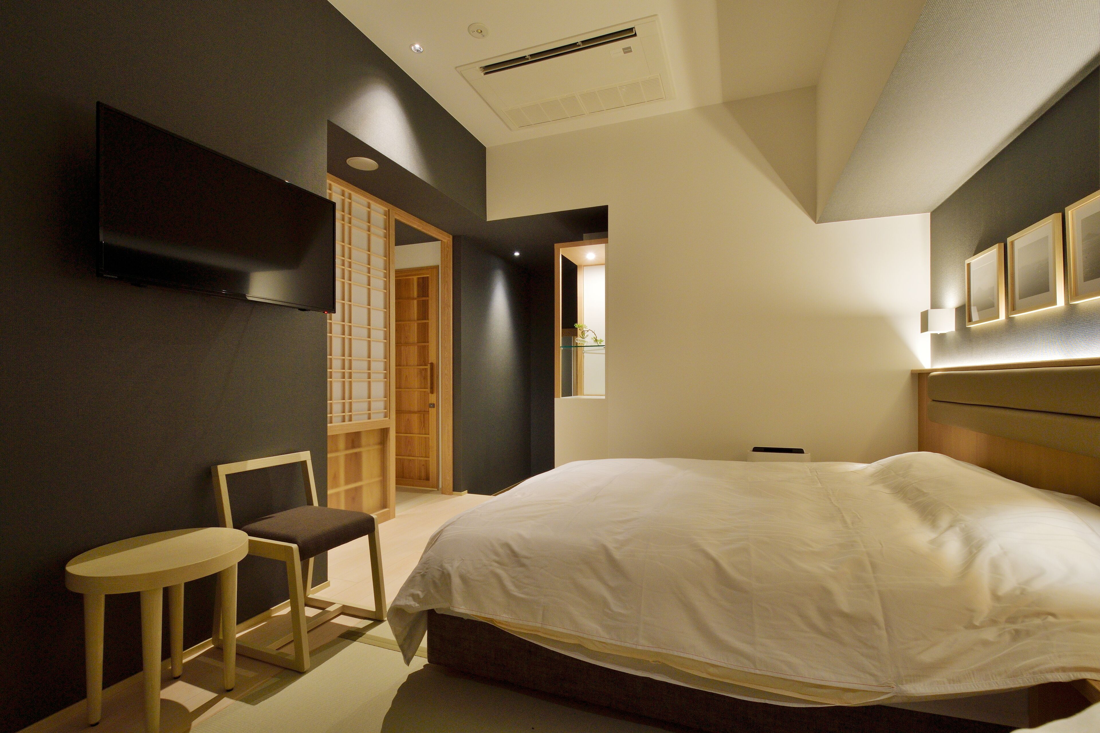 Un dormitorio moderno con una cama grande, un televisor montado en la pared, una mesita y una silla.