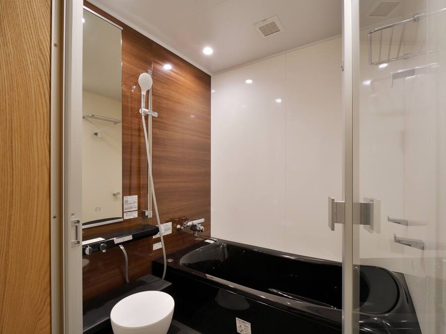 A modern bathroom with a glass shower enclosure, a black bathtub, and a wooden vanity.