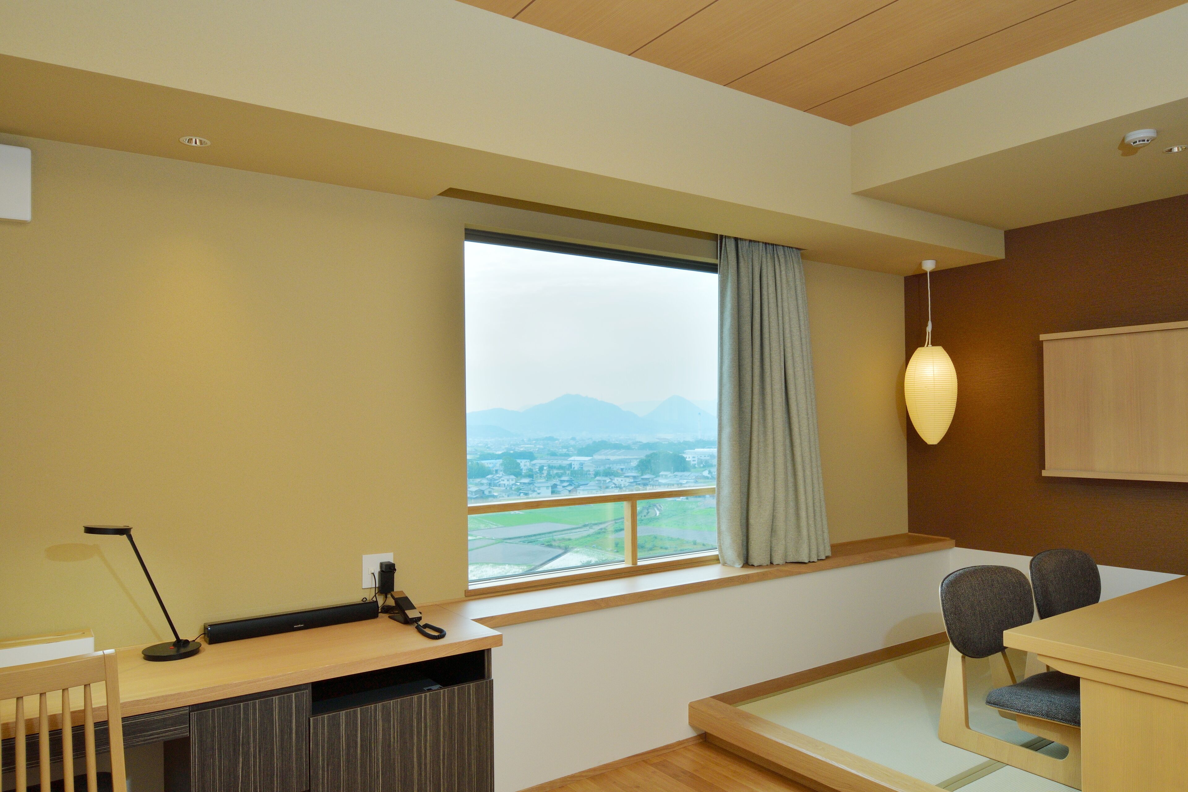 Une chambre d’hôtel avec une grande fenêtre, un bureau, une chaise et un lit.