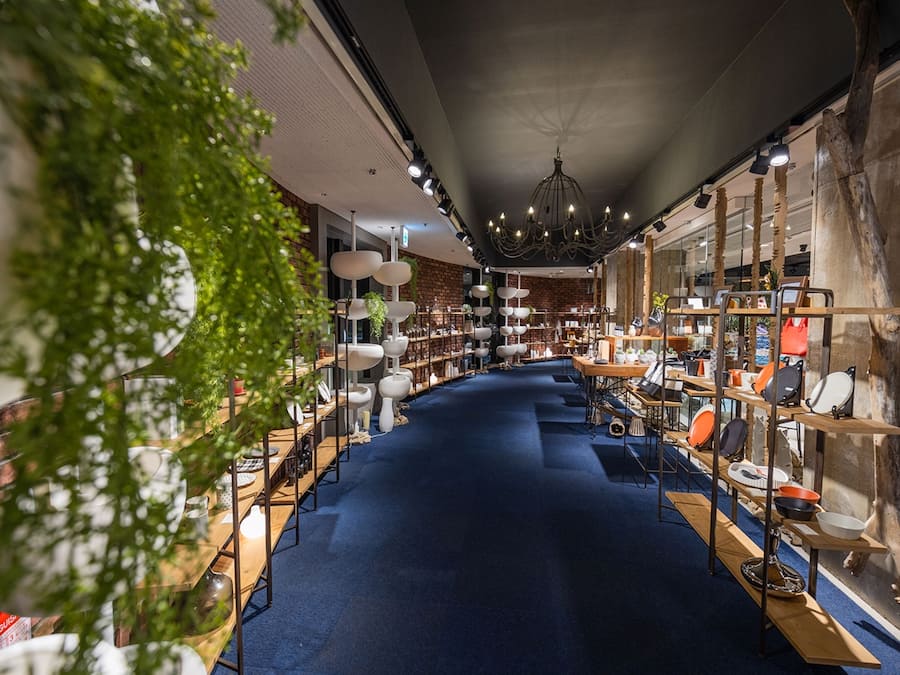 A modern interior with a central blue carpet, wooden tables, and shelves displaying various items.