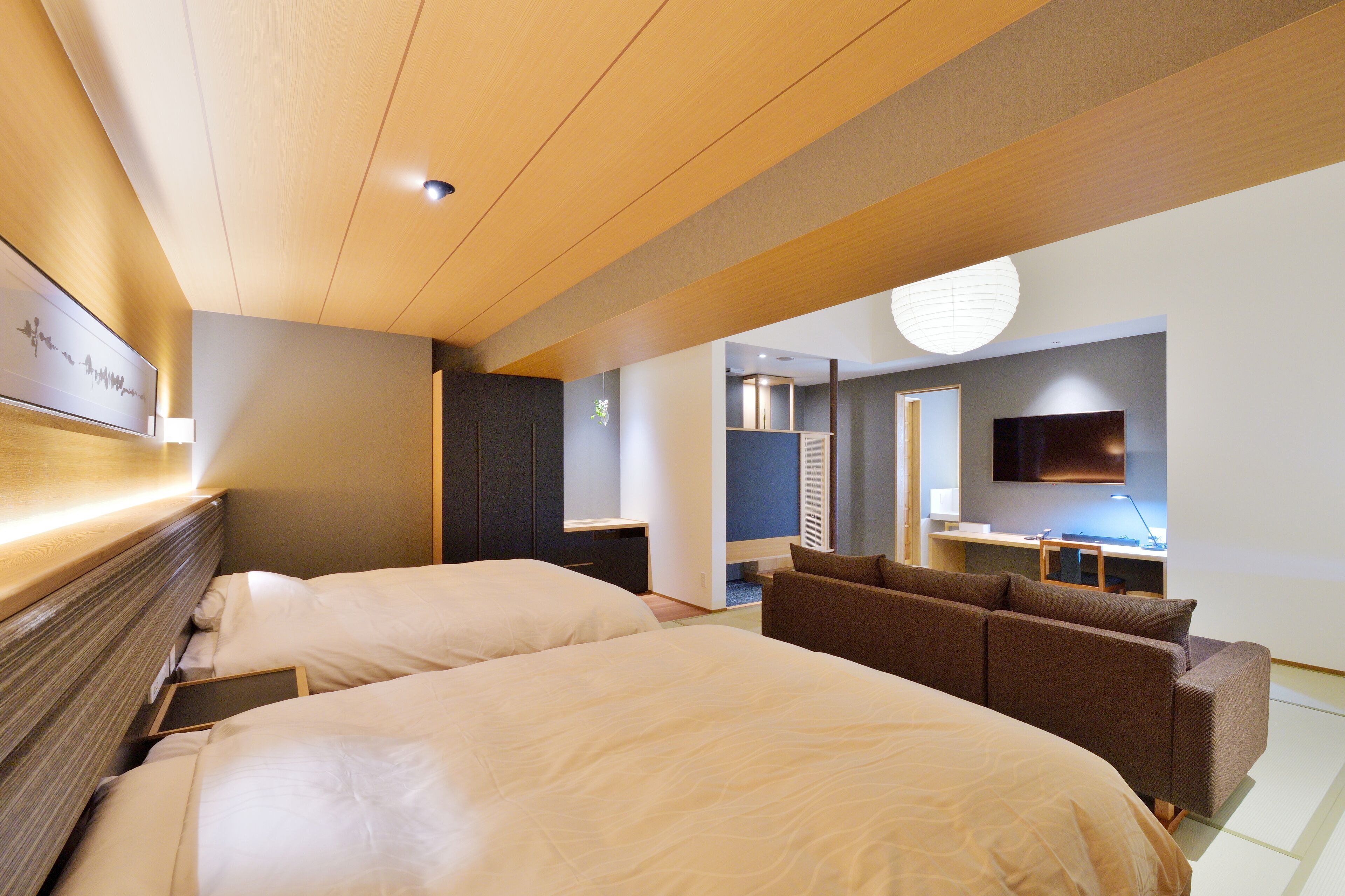 Ein Hotelzimmer mit zwei Betten, einem Schlafsofa, einem Schreibtisch, einem Flachbildfernseher und einem an der Wand montierten Fernseher.