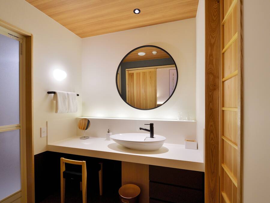 Uma casa de banho moderna com teto de madeira, um espelho redondo, uma pia branca e um porta-toalhas.