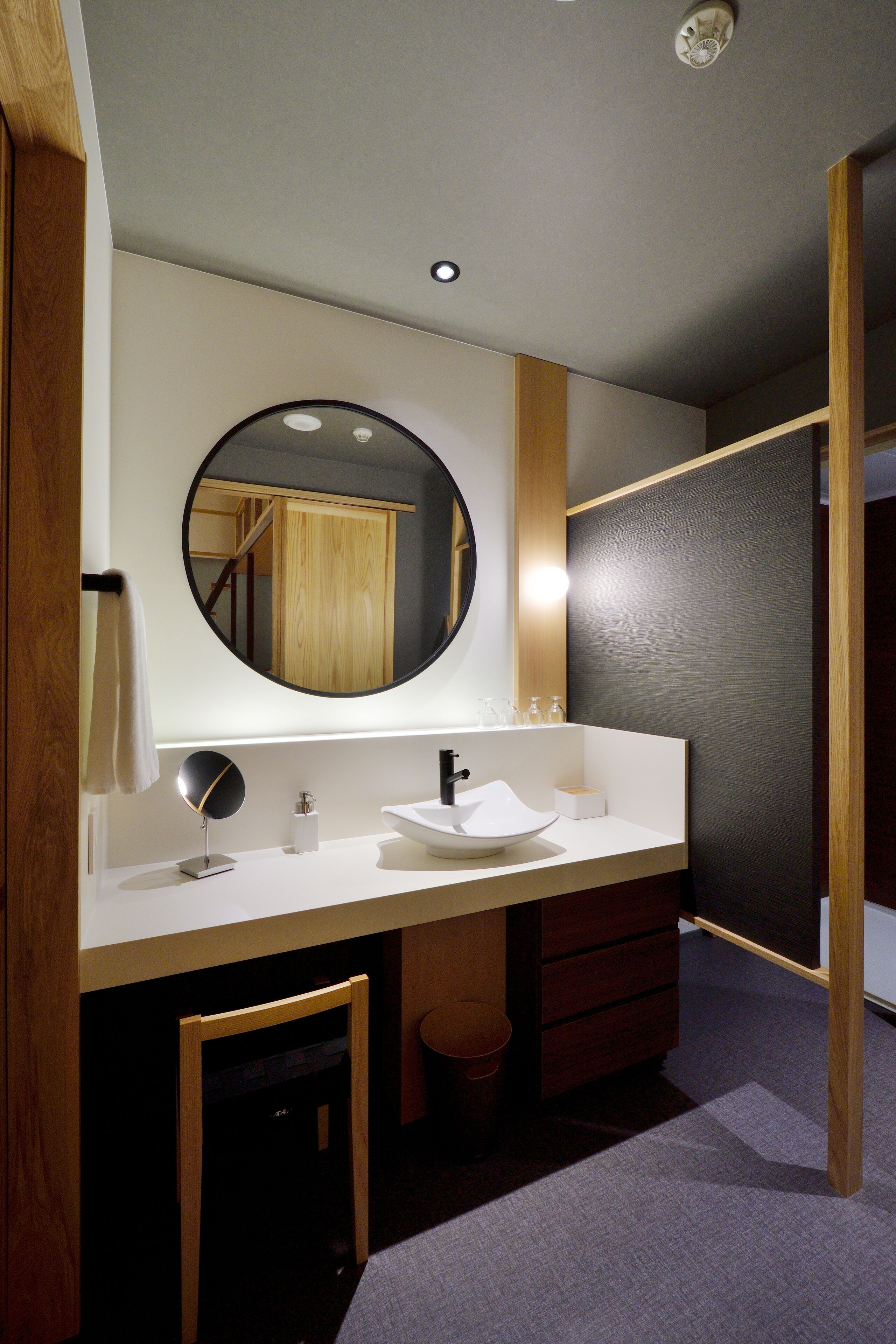 Un baño moderno con un espejo redondo, lavamanos blanco y un mueble de madera.