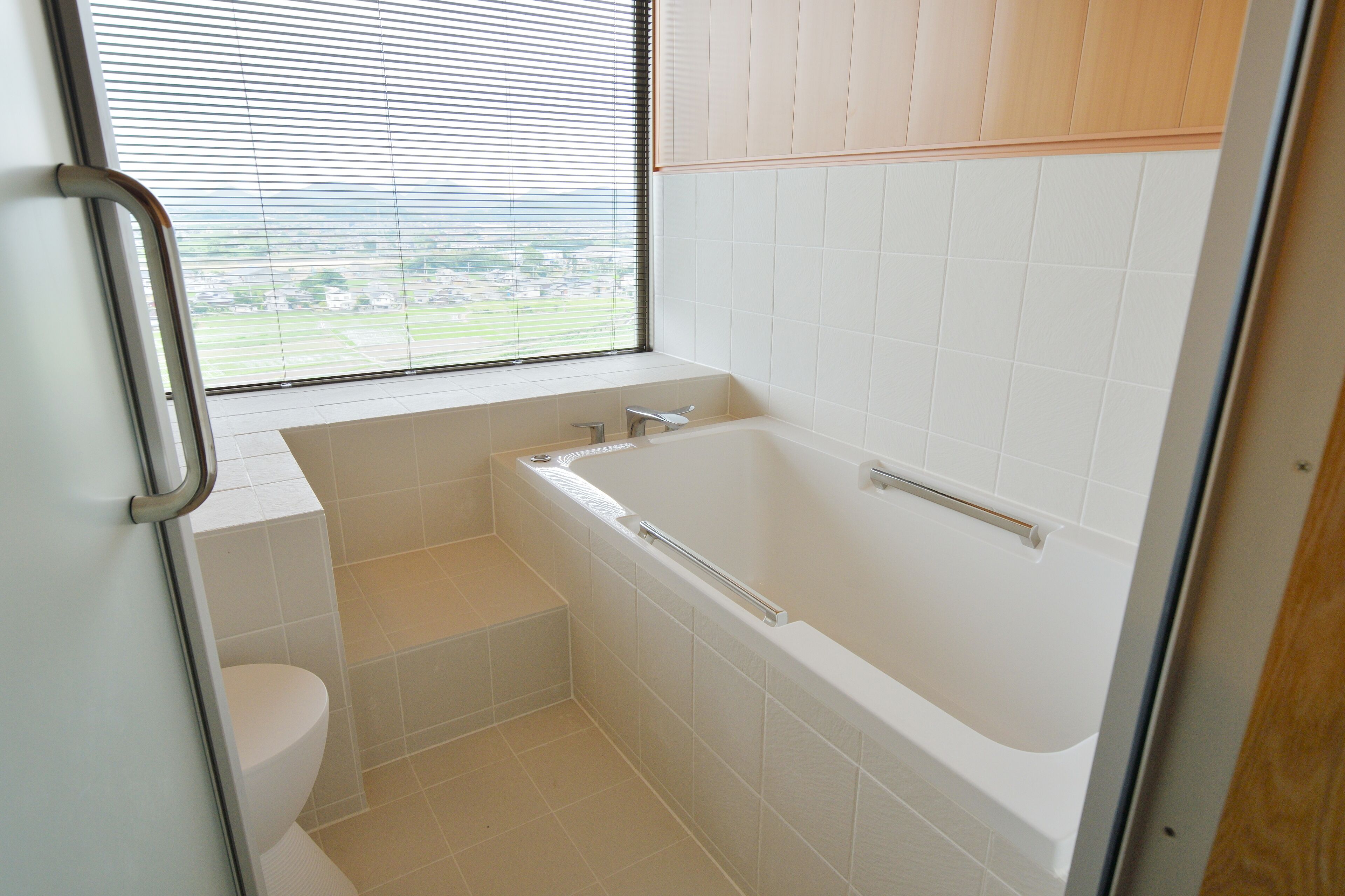 A bathroom with a bathtub, toilet, and a window with blinds.