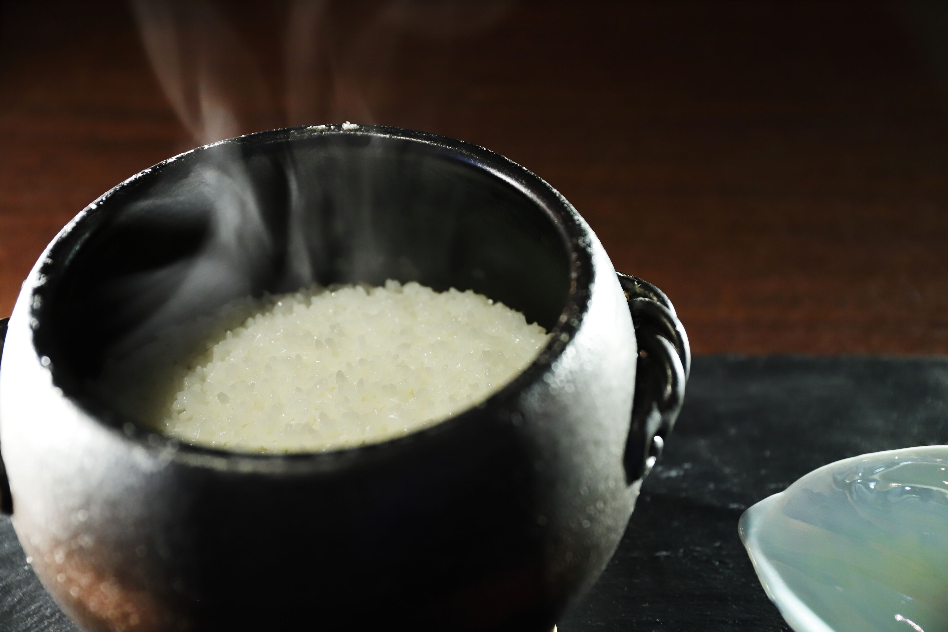 A black ceramic bowl filled with white rice on a dark surface.