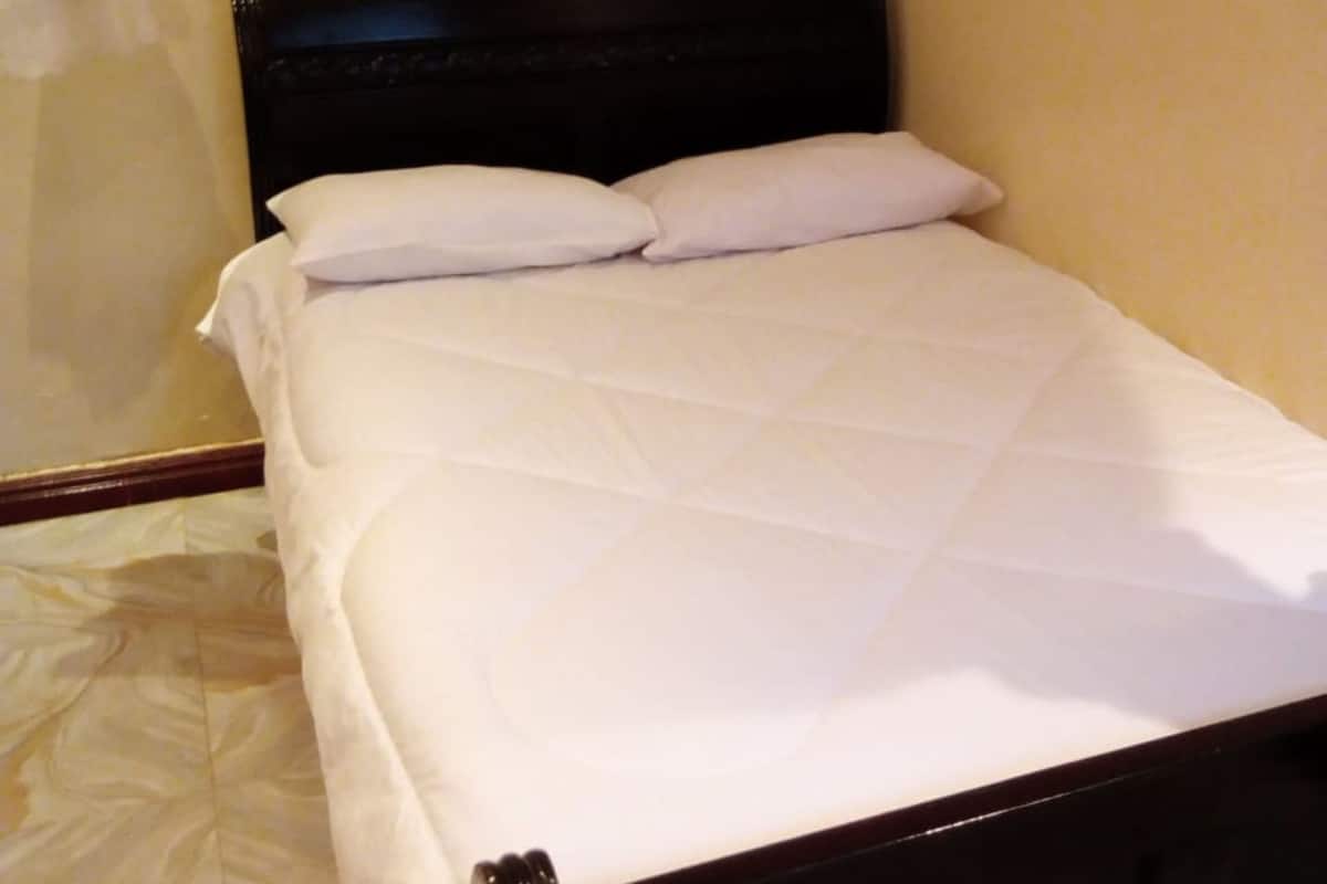 A single bed with a black headboard and white bedding in a room with plain walls and a patterned floor.