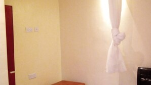 A hotel room with a bed, a small wooden table, a wall-mounted curtain, and a ceiling light. - Silver Hotel Kisumu (Kisumu)