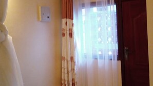 A room with a bed, a door, and a window with curtains. - Silver Hotel Kisumu (Kisumu)