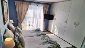 A bedroom with a bed, a TV mounted on the wall, and a wardrobe. - Blue Mountain Guest House (Cape Town)