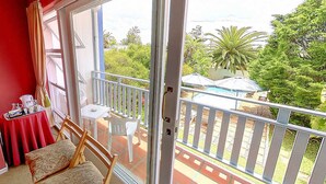 A balcony with a table and chairs, a sliding glass door, and a view of a garden with a pool. - Blue Mountain Guest House (Cape Town)