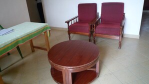 A room with a round wooden table, two wooden chairs with red cushions, and a green-striped tablecloth on a wooden table. - Cawaal Hotels (Kisumu)