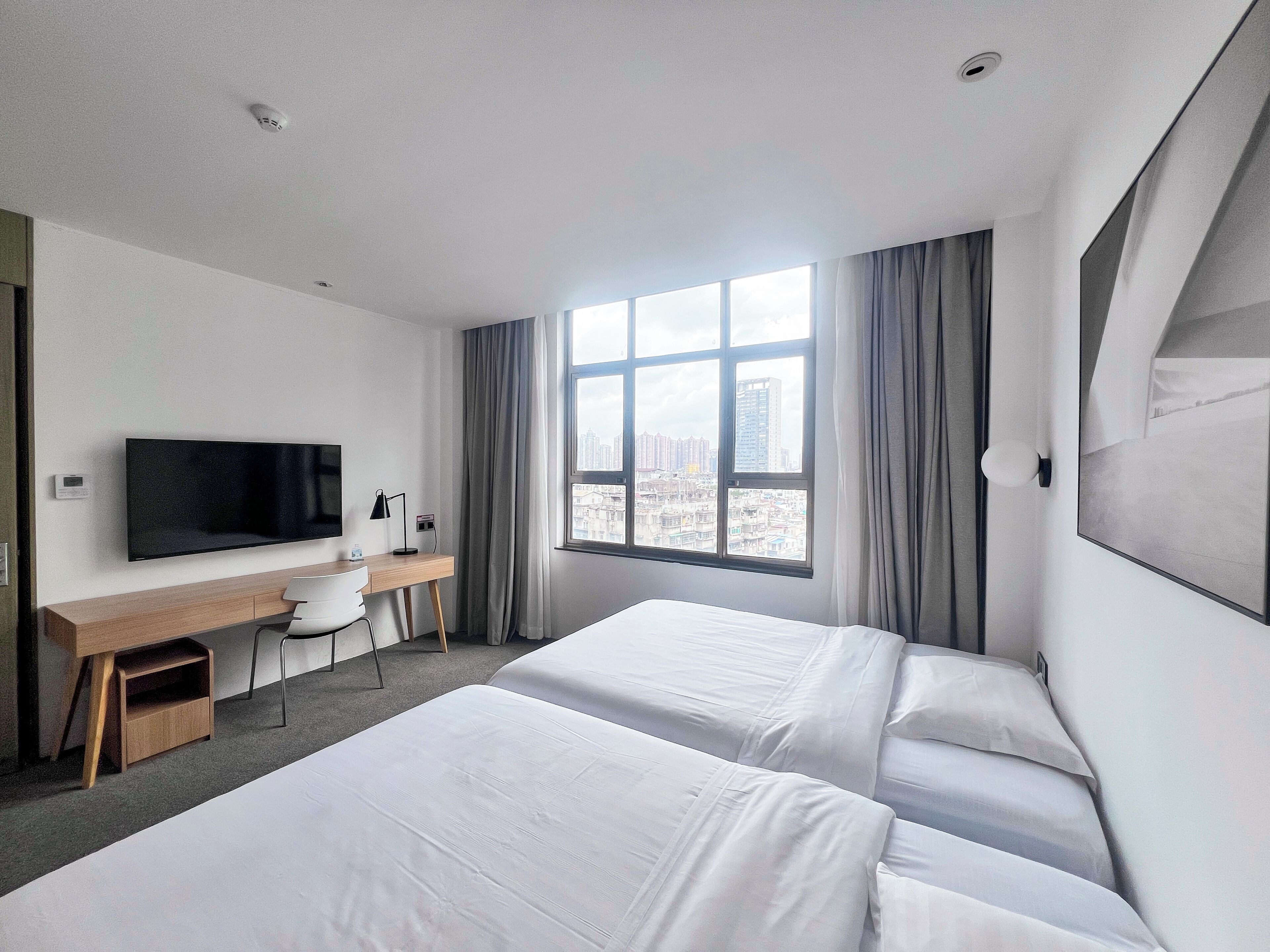 Una habitación de hotel con dos camas, un escritorio con silla, un televisor y una ventana con cortinas.