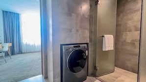 A modern bathroom with a built-in washer and dryer, a shower, and a small seating area with a table and chair. - LN Residence Guangzhou Changdi - Free shuttle between hotel and Exhibition Center during Canton Fair (Guangzhou)