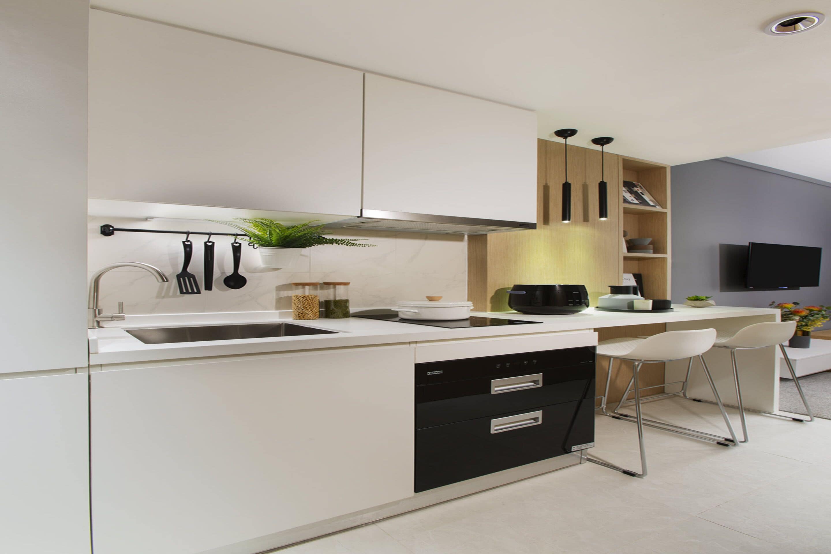 A modern kitchen with a white countertop, black appliances, and a built-in oven. There are two white bar stools and a potted plant.