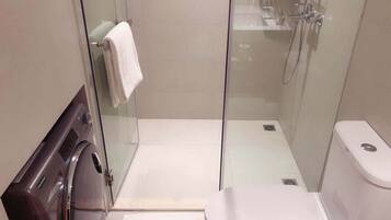 A modern bathroom with a glass-enclosed shower, a toilet, and a washing machine.