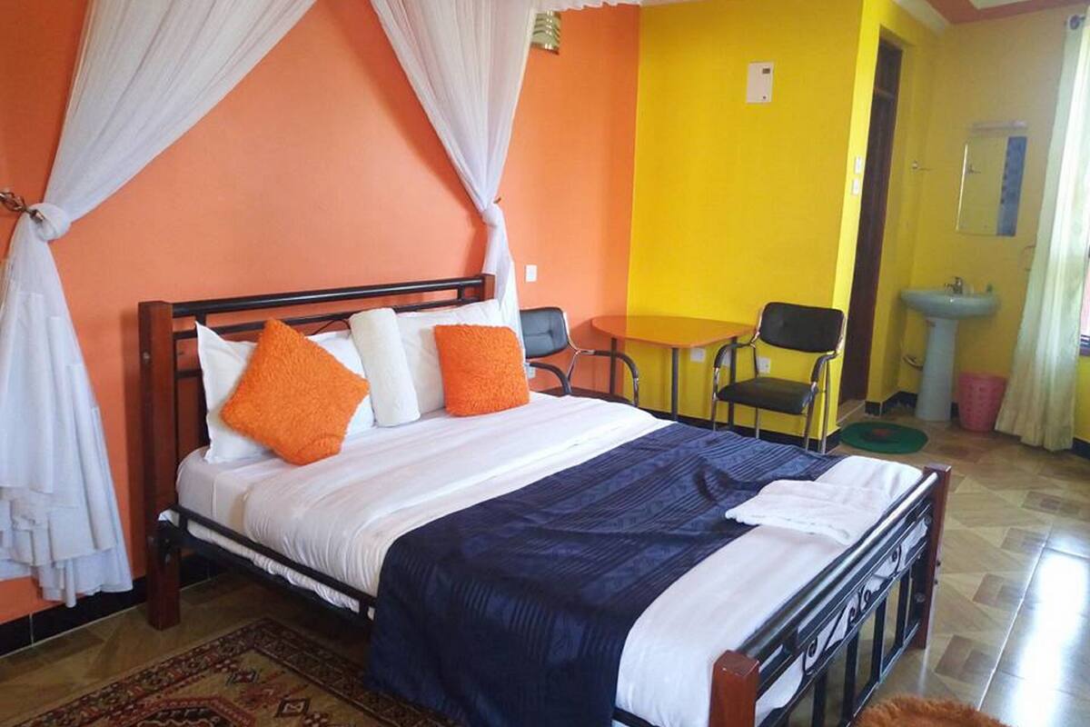 A bed with white and orange pillows, a blue blanket, and a canopy. There is a small table and two chairs in the corner.