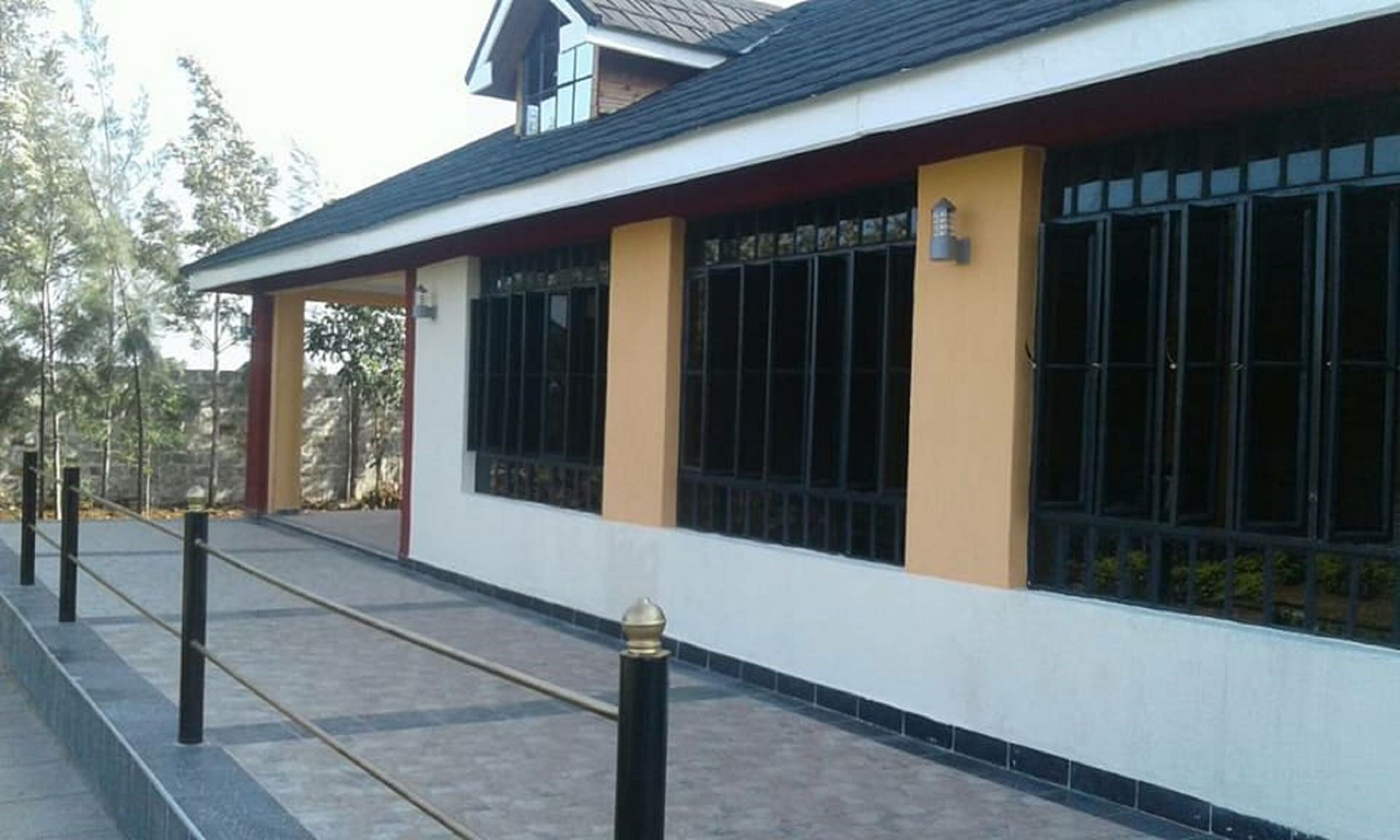 Ein Gebäude mit einer überdachten Veranda, großen Fenstern mit Metallgitter und einer gelben Fassade.