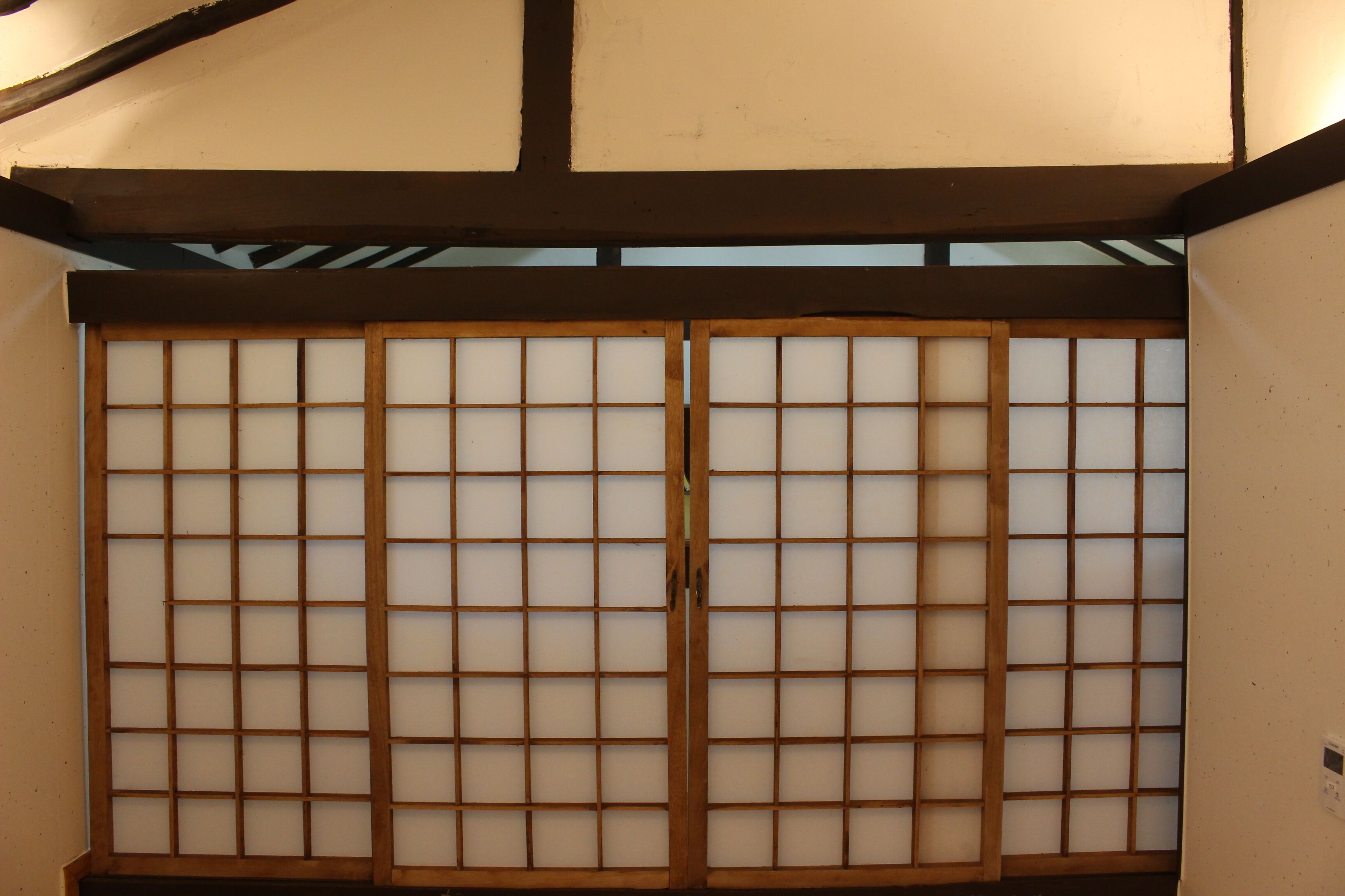A traditional Japanese room with tatami flooring, a shoji screen door, and a low ceiling with exposed beams.