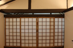 A traditional Japanese room with tatami flooring, a shoji screen door, and a low ceiling with exposed beams. - BongHwangJae Hanok (Gongju)