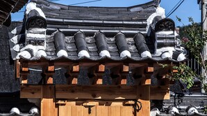 Une porte en bois traditionnelle, surmontée d’un toit en tuiles, qui se dresse devant un mur de briques.