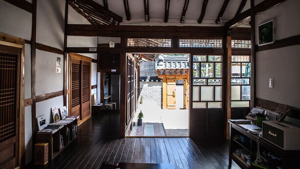 Un intérieur japonais traditionnel avec un sol recouvert de tatamis, des poutres en bois, des portes coulissantes et une vue sur l’extérieur.