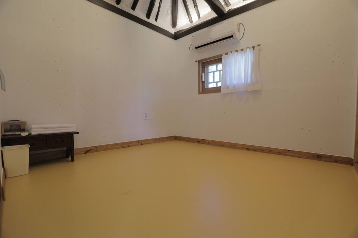 Une pièce avec un plafond en pente, une petite fenêtre avec des rideaux, un banc en bois et une armoire blanche.
