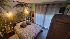 Une chambre à coucher comprenant un lit, une table de chevet, une lampe, un téléviseur fixé au mur et une fenêtre avec des rideaux.