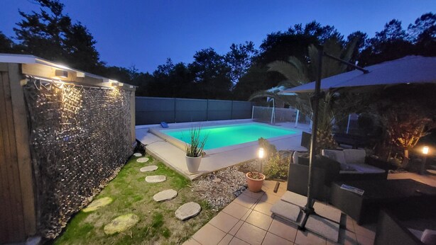 Un jardin avec une piscine, un mur en pierre, des plantes en pot et du mobilier d’extérieur.