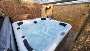 Un bain à remous doté d’un panneau de commande, entouré de murs en bois et surmonté d’une terrasse en bois.
